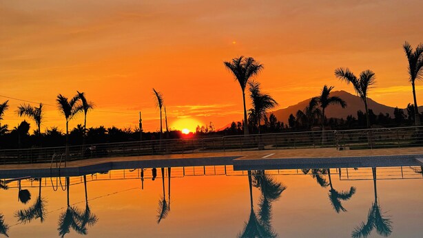 A pool reflecting palm trees and a sunset with a mountain in the background. - Casa Hacienda Las Palmeras (Patapo)