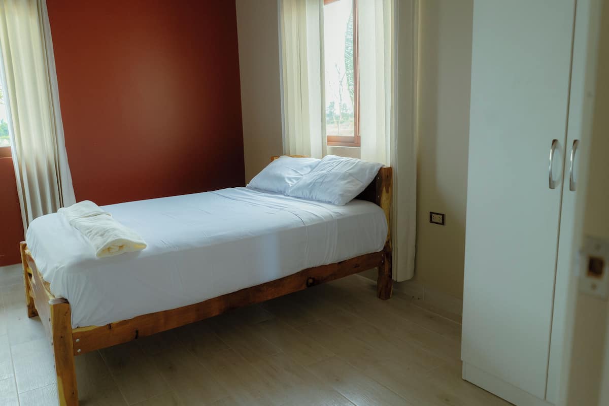 Ein Einzelbett mit weißer Bettwäsche in einem Zimmer mit Holzboden und einem weißen Kleiderschrank.