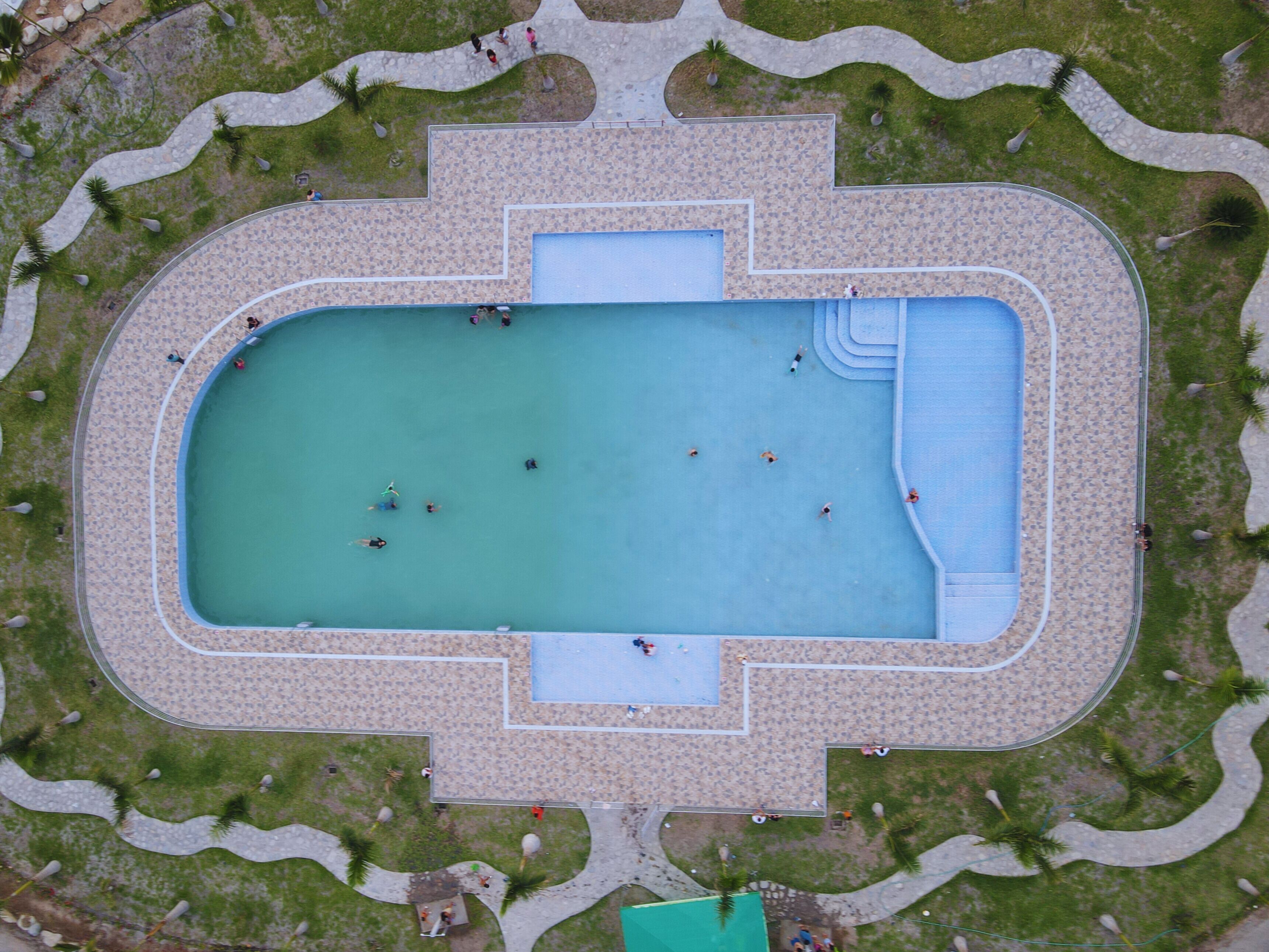 Vista aérea de una piscina rectangular con solárium circundante, rodeada de áreas ajardinadas y senderos.