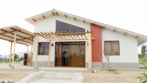 A modern house with a covered porch, large sliding glass doors, and a stone foundation. - Casa Hacienda Las Palmeras (Patapo)