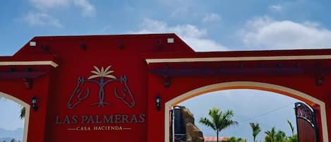 A red archway with the text "Las Palmeras Casa Hacienda" and a horse logo.