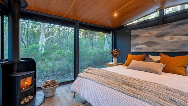 A bedroom with a large bed, a wooden ceiling, a wall-mounted painting, and a wood-burning stove. - The Hollows - Kangaroo Valley (Kangaroo Valley)