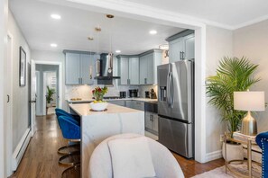 A modern kitchen with grey cabinets, stainless steel appliances, and a central island with bar stools. - Stylish 3BR Near NYC Train Parking + EV Charger (Maplewood)