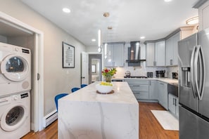 A modern kitchen with a marble island, stainless steel appliances, and a view into the adjacent laundry room.