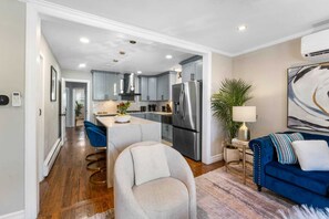 A modern kitchen with stainless steel appliances, a central island, and a dining area with blue chairs. - Stylish 3BR Near NYC Train Parking + EV Charger (Maplewood)