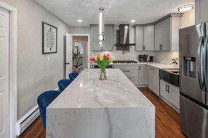 A modern kitchen with a marble island, stainless steel appliances, and a herringbone tile backsplash.