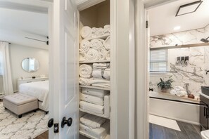 A hotel room with a neatly organized bathroom, a bed with a white headboard, and a large mirror. - Stylish 3BR Near NYC Train Parking + EV Charger (Maplewood)