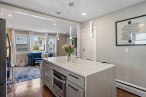 A modern kitchen with a marble island, stainless steel appliances, pendant lighting, and a large window offering a view of the outside.