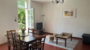 A dining area with a wooden table and chairs, a television on a stand, a small rug, and a framed picture on the wall. - House in the village, near Avignon (Barbentane)