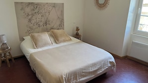 A bedroom with a large bed, two pillows, a nightstand with a lamp, a wall art piece, and a window with blinds. - House in the village, near Avignon (Barbentane)