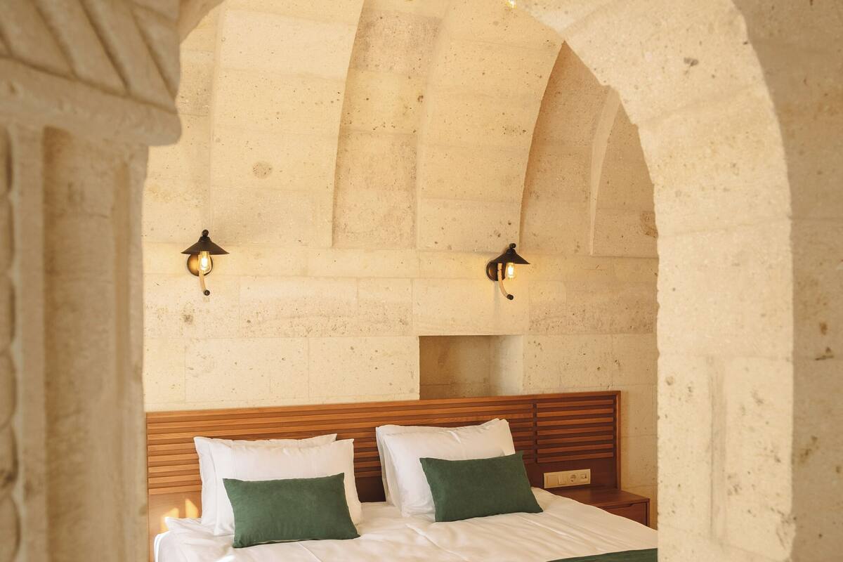 Un dormitorio con cama de madera, ropa de cama verde y blanca, y dos lámparas de pared.