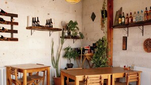 A rustic dining area with wooden tables and chairs, hanging plants, and shelves with bottles. - Juno Cappadocia (Nevsehir)