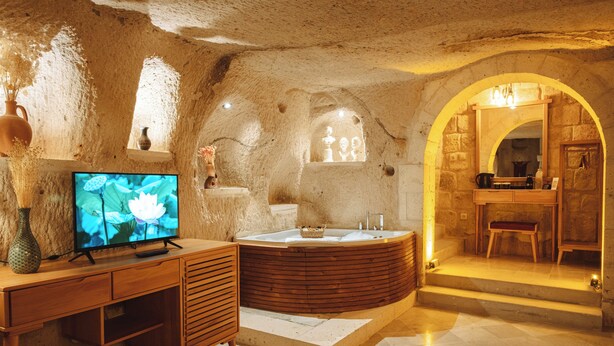 A spa room with a wooden desk, a large TV, a hot tub, and a stone wall. - Juno Cappadocia (Nevsehir)