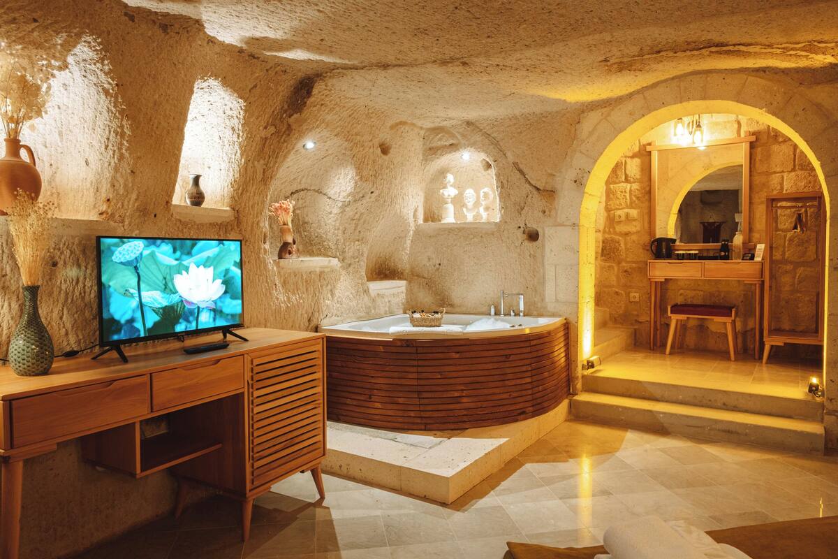Una sala de spa con un escritorio de madera, un televisor grande, un jacuzzi y una pared de piedra.