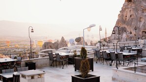 An outdoor seating area with tables and chairs, a potted plant, and a rocky backdrop. - Juno Cappadocia (Nevsehir)