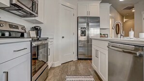 A modern kitchen with stainless steel appliances, white cabinetry, and a wooden floor.