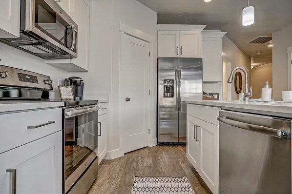 A modern kitchen with stainless steel appliances, white cabinetry, and a wooden floor.