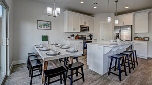 A modern kitchen with white cabinetry, a central island with stools, and a dining area with a long table set for six.