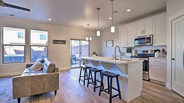 A modern kitchen with white cabinets, a central island with stools, a microwave, and a sink.