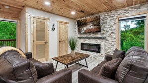 Ein gemütlicher Wohnbereich mit Kamin aus Stein, Ledersofas und Holzboden.
