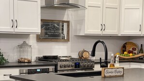 Cocina moderna con armarios blancos, estufa de acero inoxidable y grifo negro. Hay dos taburetes de bar y un letrero que dice 'Choose Happy'.