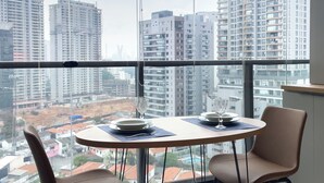 Un apartamento en un rascacielos con un amplio ventanal, una mesa de comedor con sillas y vistas a edificios circundantes.