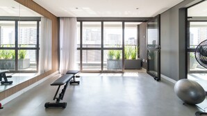 Un gimnasio moderno con equipo de ejercicio, ventanas amplias y plantas en macetas.