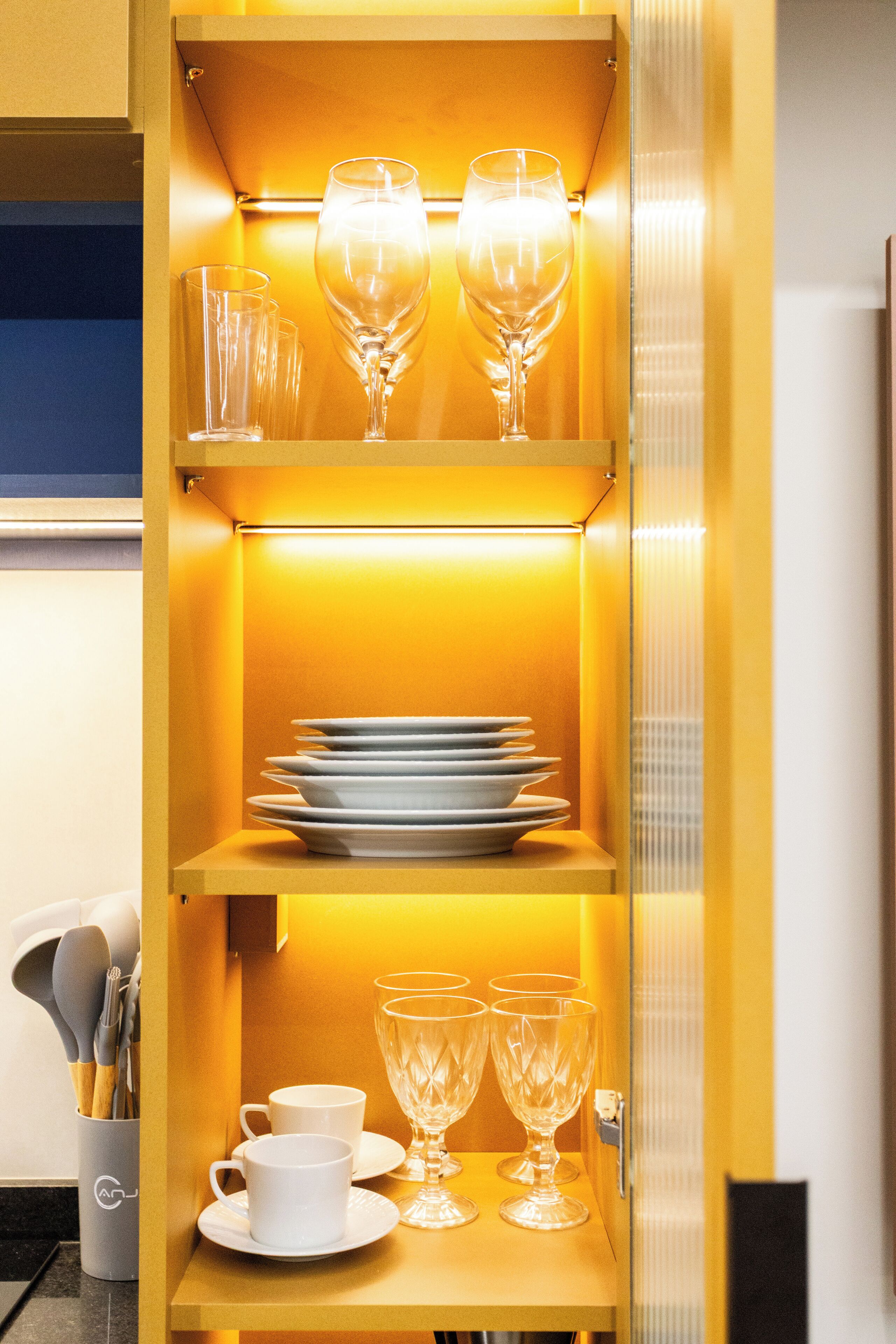 A well-lit, modern kitchen area with a built-in shelf unit holding plates, glasses, and a set of utensils.