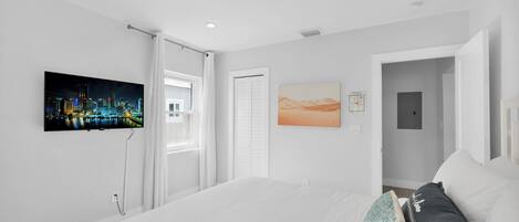 A modern hotel room with a large bed, a cityscape painting, a desert landscape painting, and a door leading to another room.