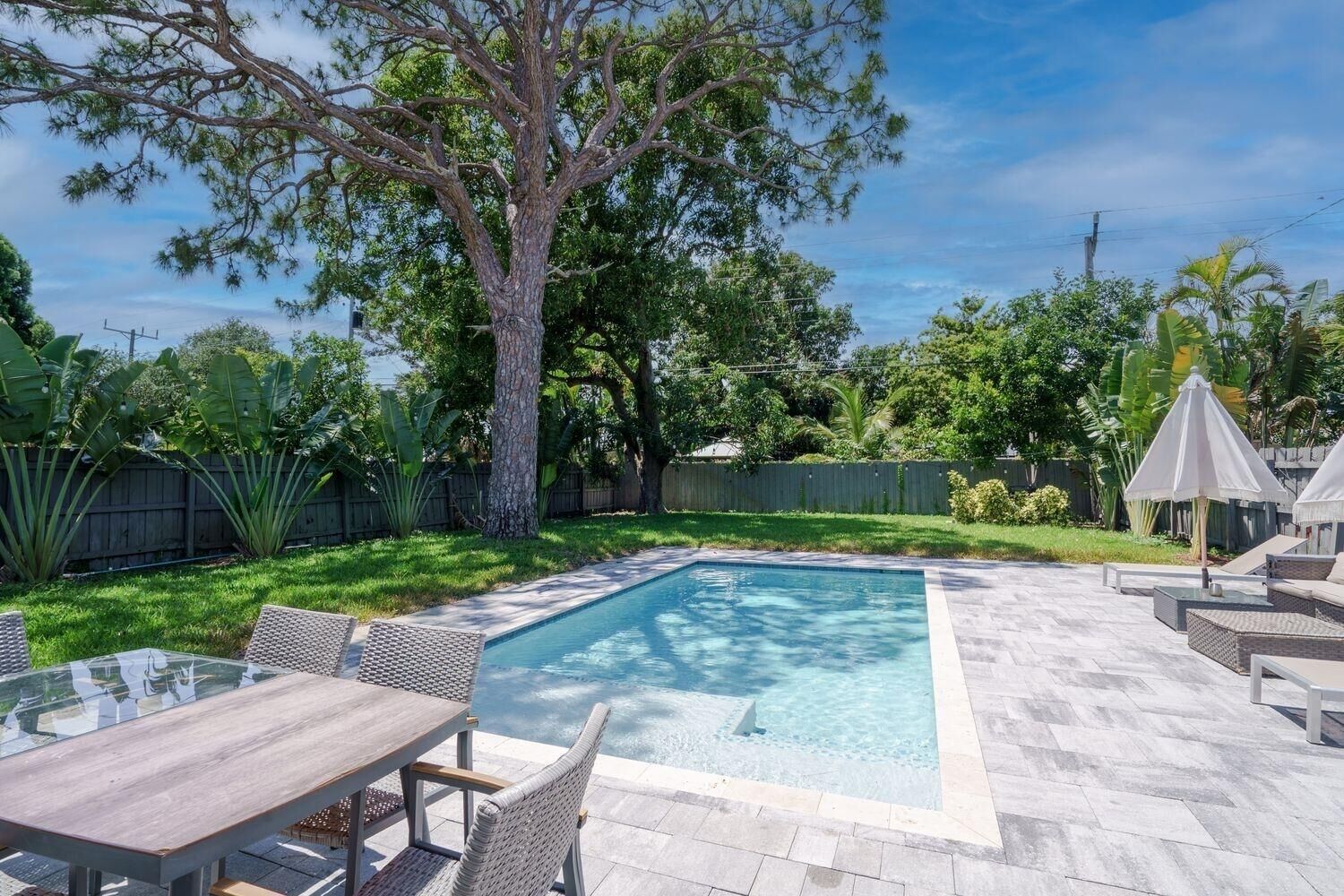 Et rektangulært swimmingpool med en stenbordering, omgivet af en terrasse med fletningsmøbler og et bord.