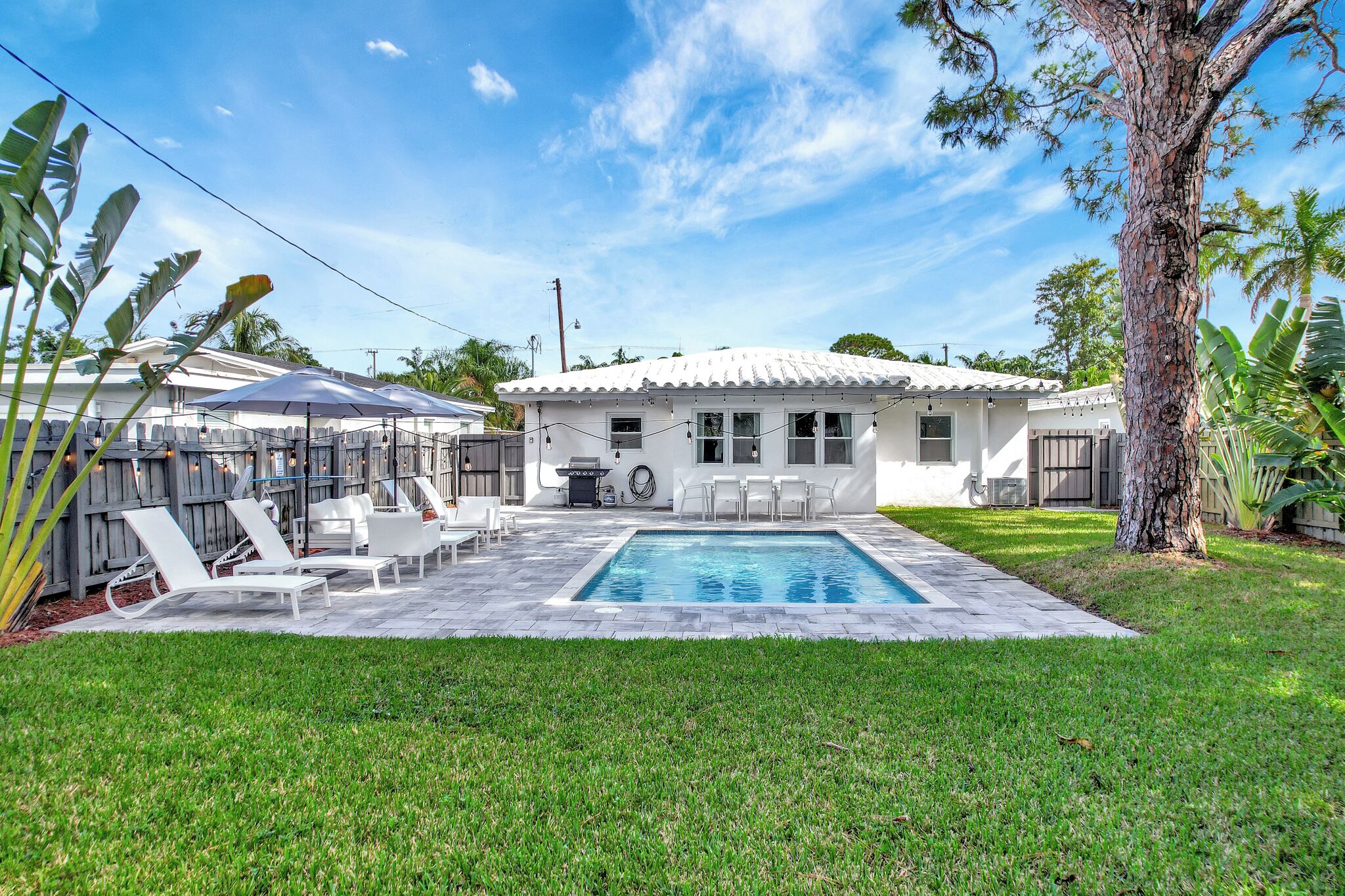 Ein Garten mit Swimmingpool, weißen Liegestühlen und einer überdachten Terrasse.
