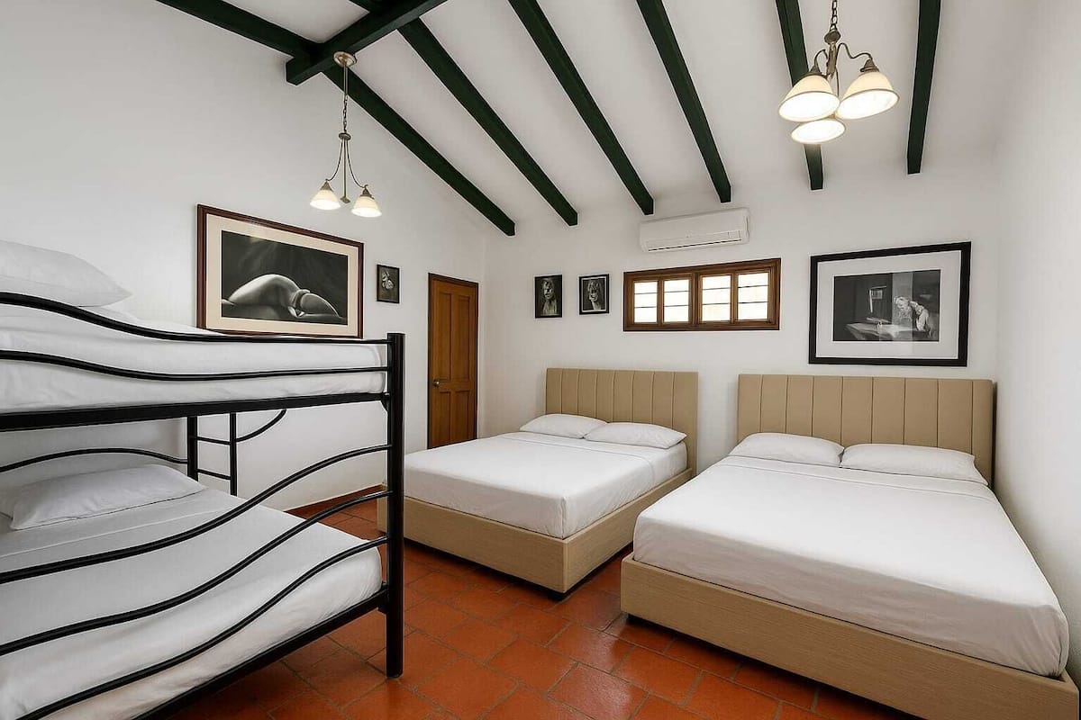 Um quarto com beliches, duas camas de solteiro, uma porta de madeira e quadros na parede.
