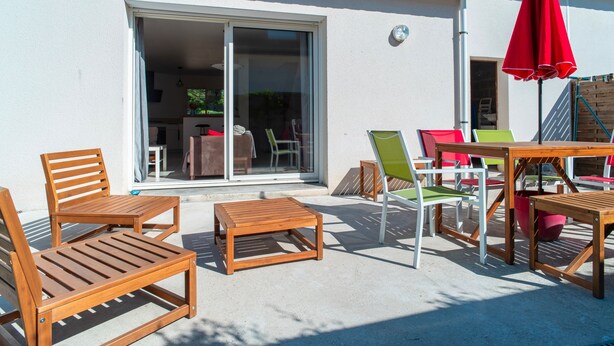 An outdoor patio with wooden furniture, a red umbrella, and a sliding glass door leading to an interior space. - Le Narbon - maison proche de la plage (Erdeven)