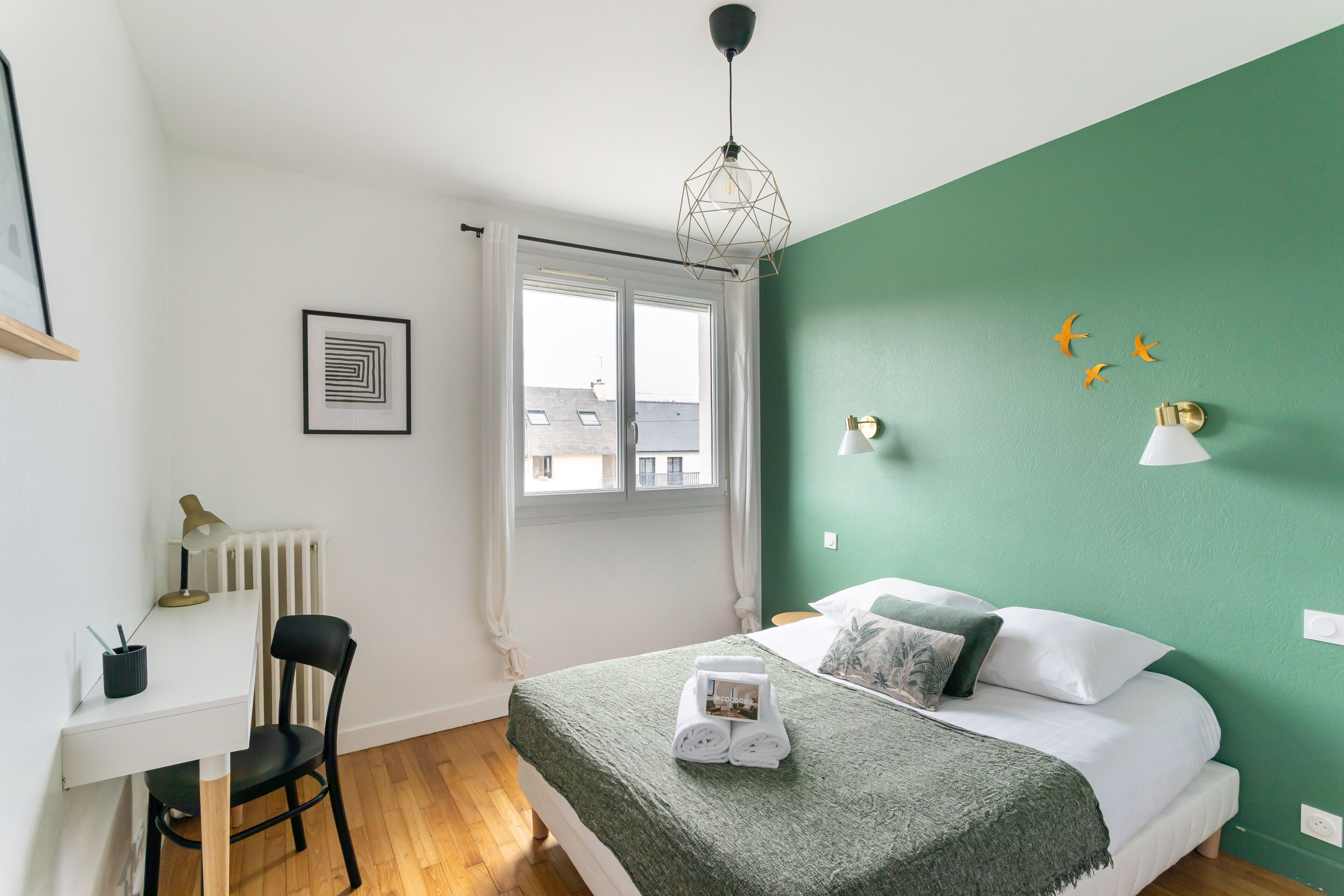 Ein Schlafzimmer mit Bett, Schreibtisch, Stuhl, Heizkörper und Fenster.