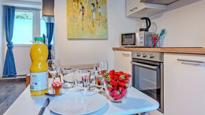 A modern kitchen with a dining table set for two, featuring a bottle of orange juice, glasses, a bowl of strawberries, and a microwave.