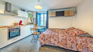 A compact kitchen with a built-in oven, a dining area with a table and chairs, and a bed with a patterned bedspread.
