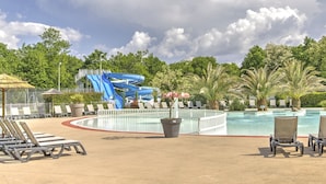 Un área de piscina con sillones de descanso, un tobogán acuático y una piscina rodeada de palmeras.