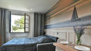 A bedroom with a bed, a small table with plates and glasses, and a painting of a sailboat on the wall. - Tom 01 - 5min à pied de la Plage (Fréhel)