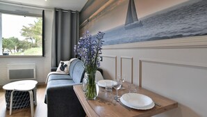 A dining area with a wooden table set for two, a vase of flowers, and a mural of a sailboat on the wall. - Tom 01 - 5min à pied de la Plage (Fréhel)