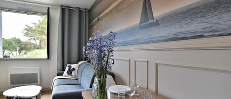 A dining area with a wooden table set for two, a vase of flowers, and a mural of a sailboat on the wall.