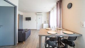 A modern kitchen with a dining table set for two, a grey sofa, and a flat-screen TV mounted on the wall.
