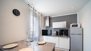 A modern kitchen with a dining table set for two, a microwave, a coffee maker, and a refrigerator.