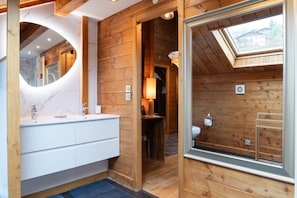 Ein Badezimmer einer Holzhütte mit einem Oberlicht, einem weißen Waschtisch und einem Spiegel.