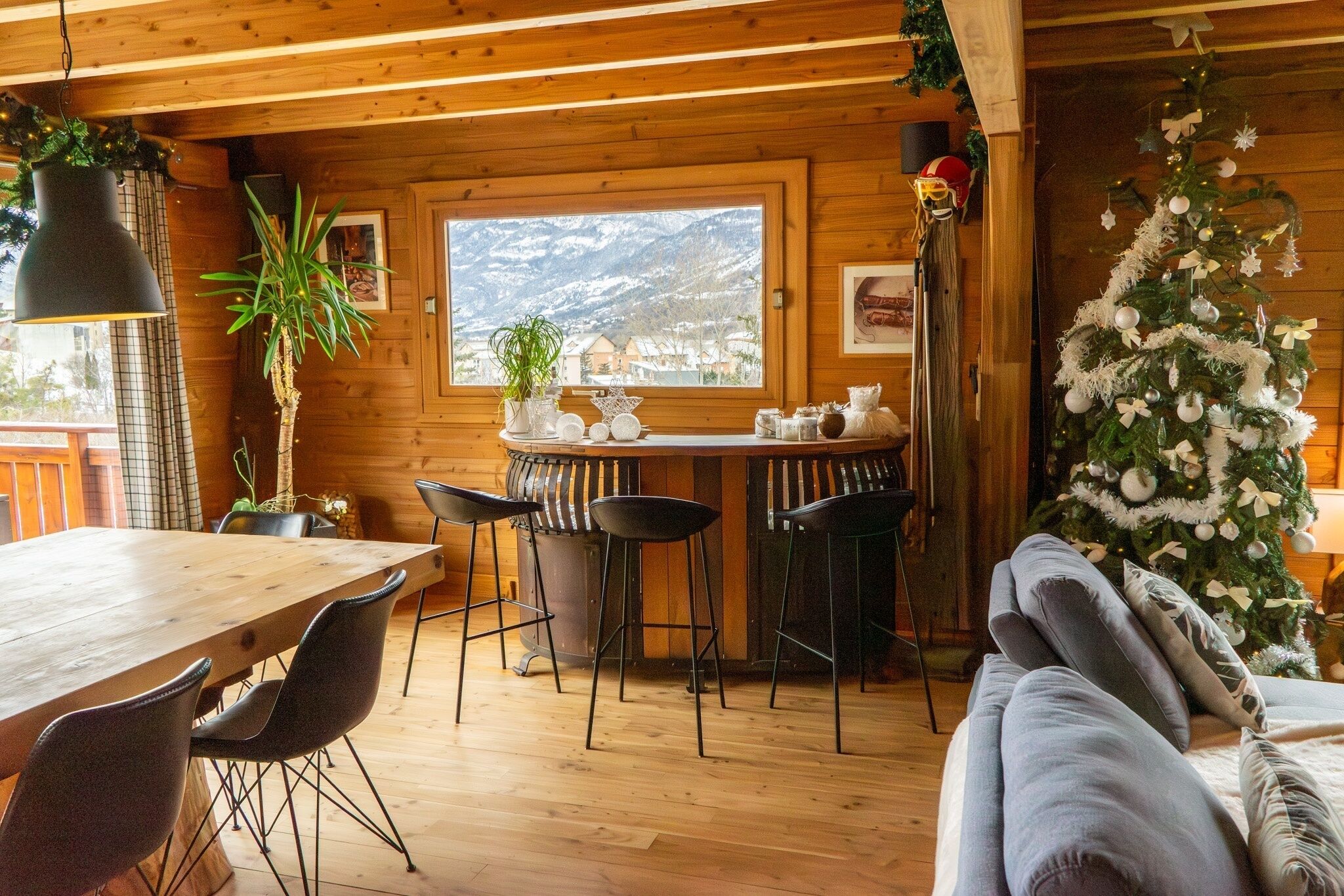 Interior de una cabaña de madera con comedor, barra y un árbol de Navidad.