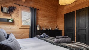 Un dormitorio de cabaña de madera con una cama, un aparador, una ventana y una puerta.