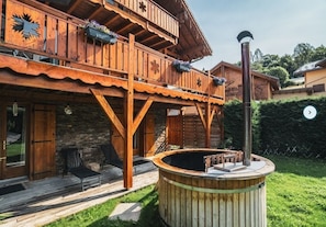 A wooden chalet with a balcony, a stone wall, and a hot tub.