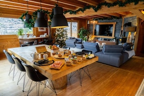 A wooden interior with a dining table, chairs, a sofa, and a TV.