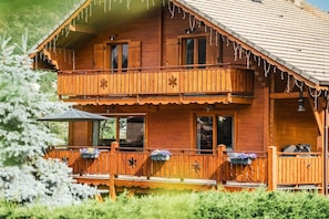 A wooden chalet with a balcony, windows, and outdoor seating.