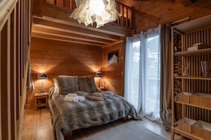 Ein gemütliches Schlafzimmer in einer Holzhütte, mit einem Bett, Nachttischlampen, einem Regal mit Gegenständen und einem Fenster mit Vorhängen.