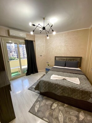 A bedroom with a bed, a ceiling light fixture, a window with curtains, and a view of buildings outside. - Sunset Hostel (Cairo)